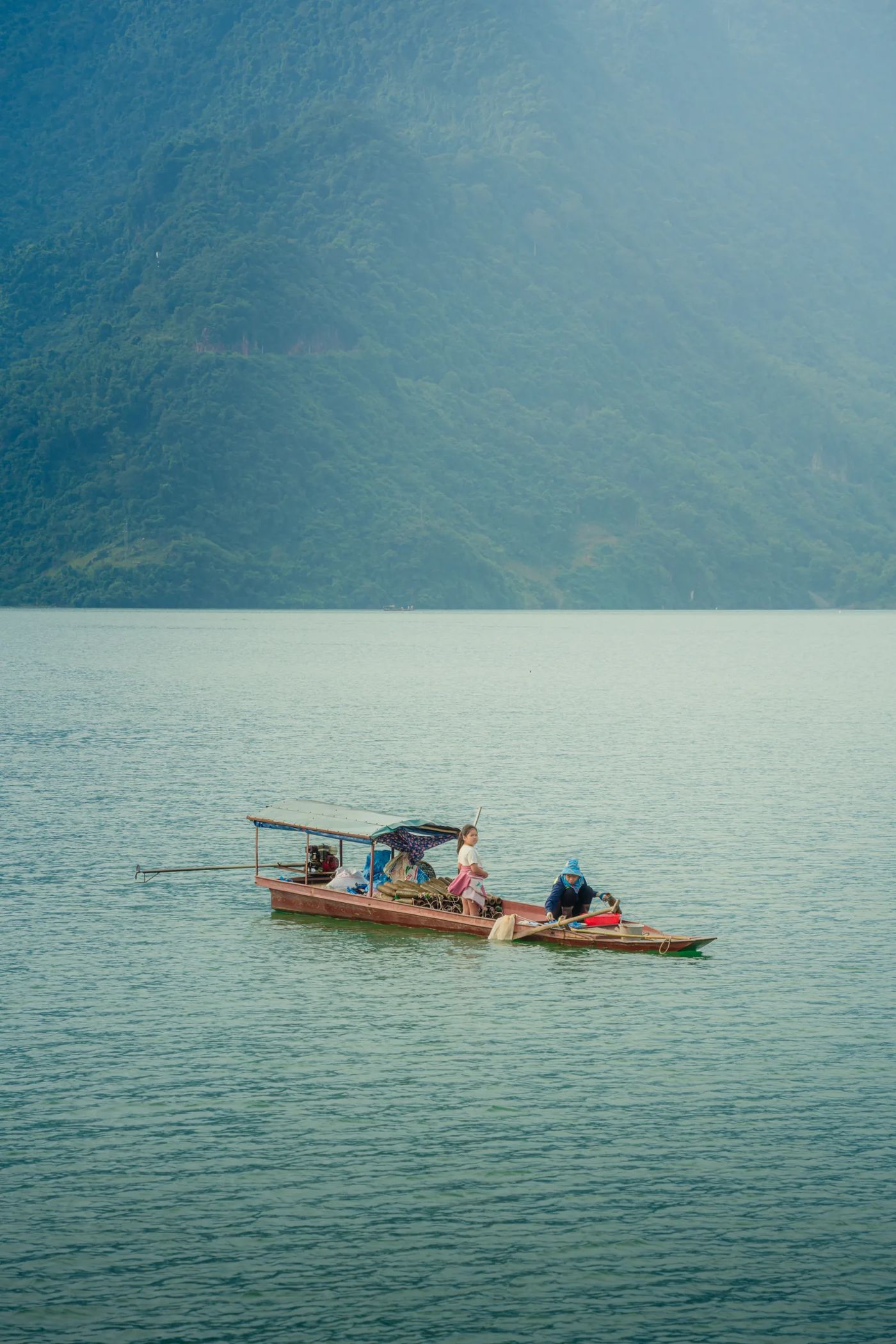 Hai người trên chiếc thuyền gỗ giữa hồ, núi rừng chìm trong sương